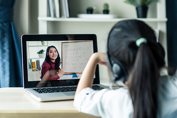 A young girl watches her teacher through a home-learning video on a computer connected to the internet.