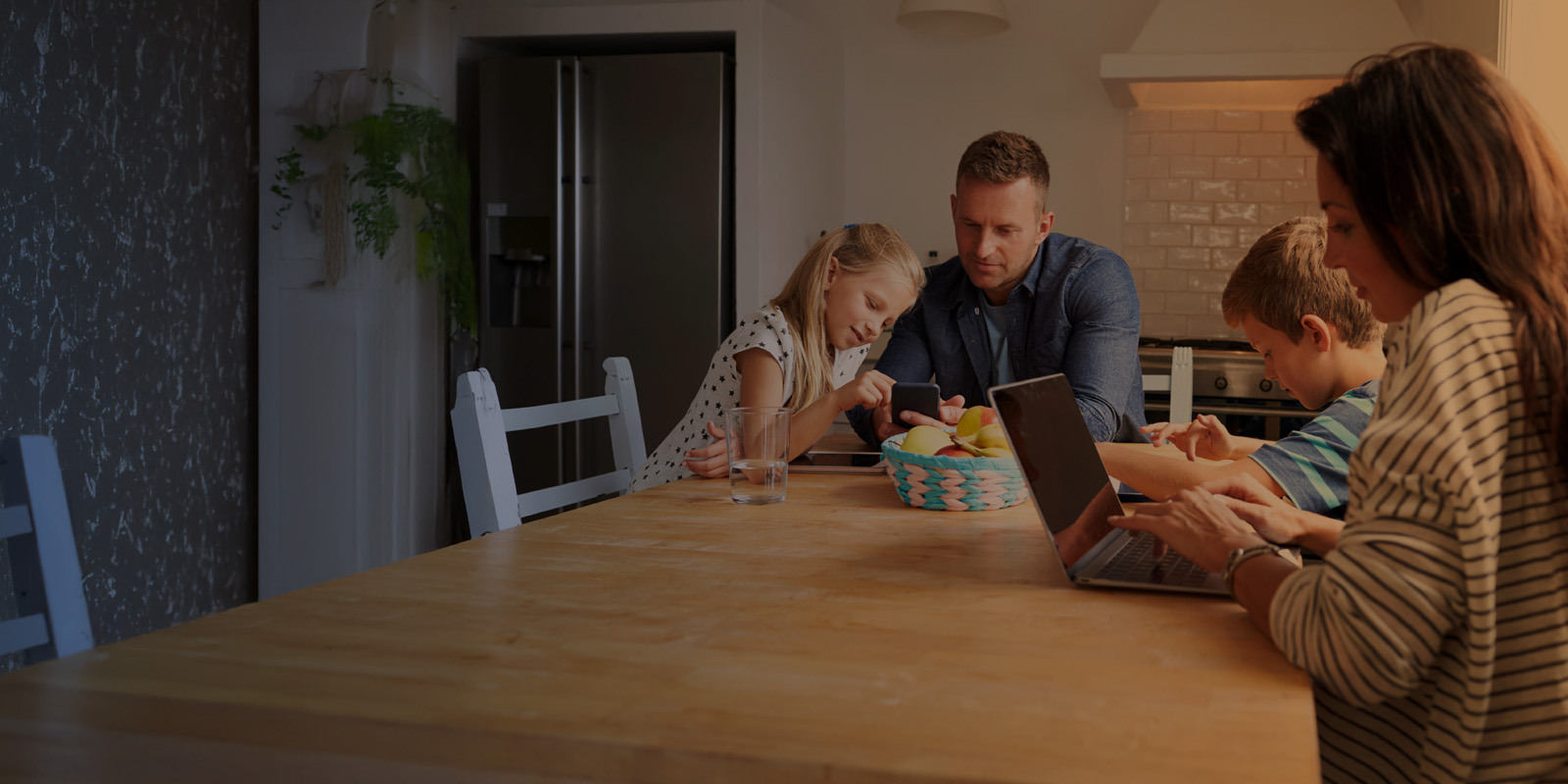 A family sits around the dinner table all using different internet connected devices.